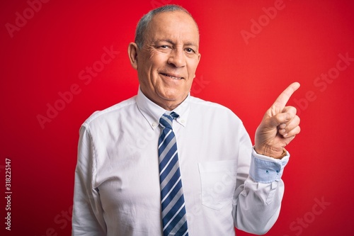 Senior handsome businessman wearing elegant tie standing over isolated red background with a big smile on face, pointing with hand and finger to the side looking at the camera.