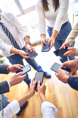 Group of business workers standing with hands together using smartphone doing symbol at the office