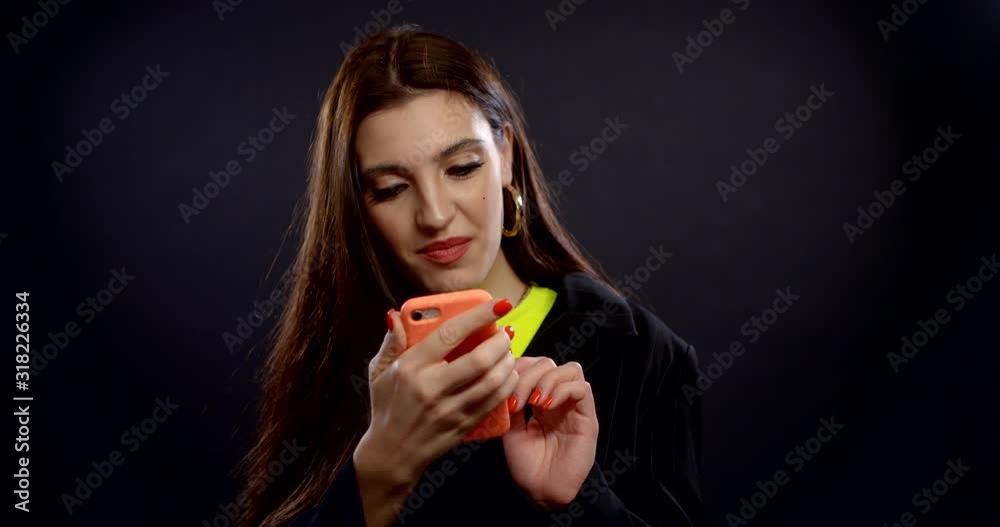 happy girl is typing message in smartphone, looks at camera and smiling broadly happy girl is typing message in smartphone, looks at camera and smiling broadly