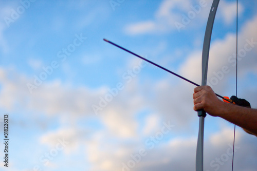 Archer's hands stretching bow and arrow pointing up in nature against the sky
