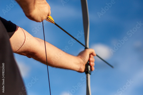 Archer's hands stretching bow and arrow pointing down in nature against the sky