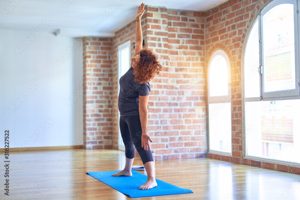 Obraz premium Middle age beautiful sportwoman on mat. Standing practicing yoga doing revolved triangle pose at gym