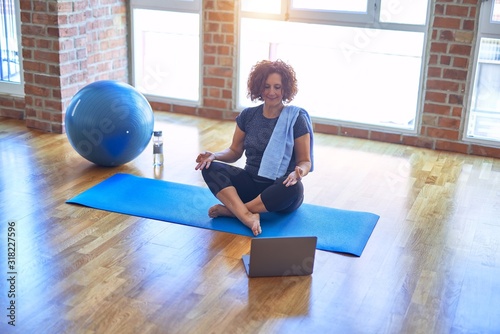 Middle age beautiful sportswoman smilig happy. Sitting on mat with smile on face using laptop at home photo