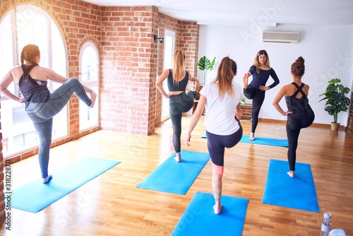 Young beautiful group of sportswomen practicing yoga. Coach teaching balance pose to sporty women at gym