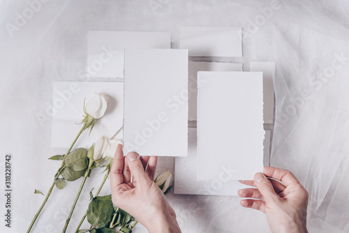 Wedding mockup. Flowers composition. White paper, elegand hand holding card, roses on white textile background. Valentine's Day. Flat lay, top view, copy space photo