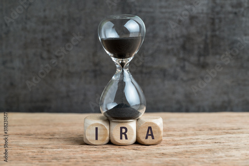 Sandglass or hourglass with black sand falling on cube wooden block with alphabet buiding the word IRA using as Individual Retirement Account concept photo