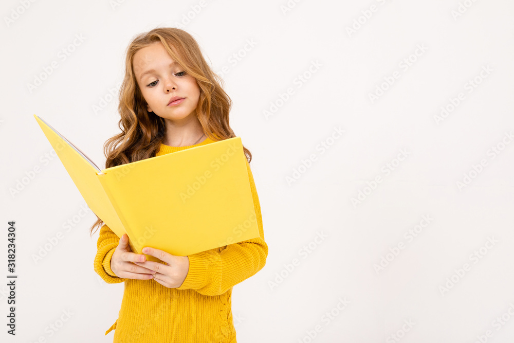 Happy teenager girl with red hair, hoody and yellow trousers read big yellow book isolated on white background Happy teenager girl with red hair, hoody and yellow trousers read big yellow book isolated on white background