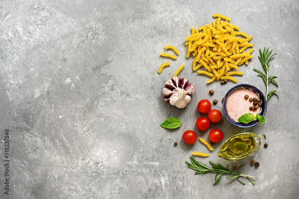 Ingredients for cooking pasta with tomato sauce. Fusilli, tomatoes, basil, olive oil, pink salt, pepper, rosemary and garlic on a gray concrete background. Top view, flat lay,copy space.