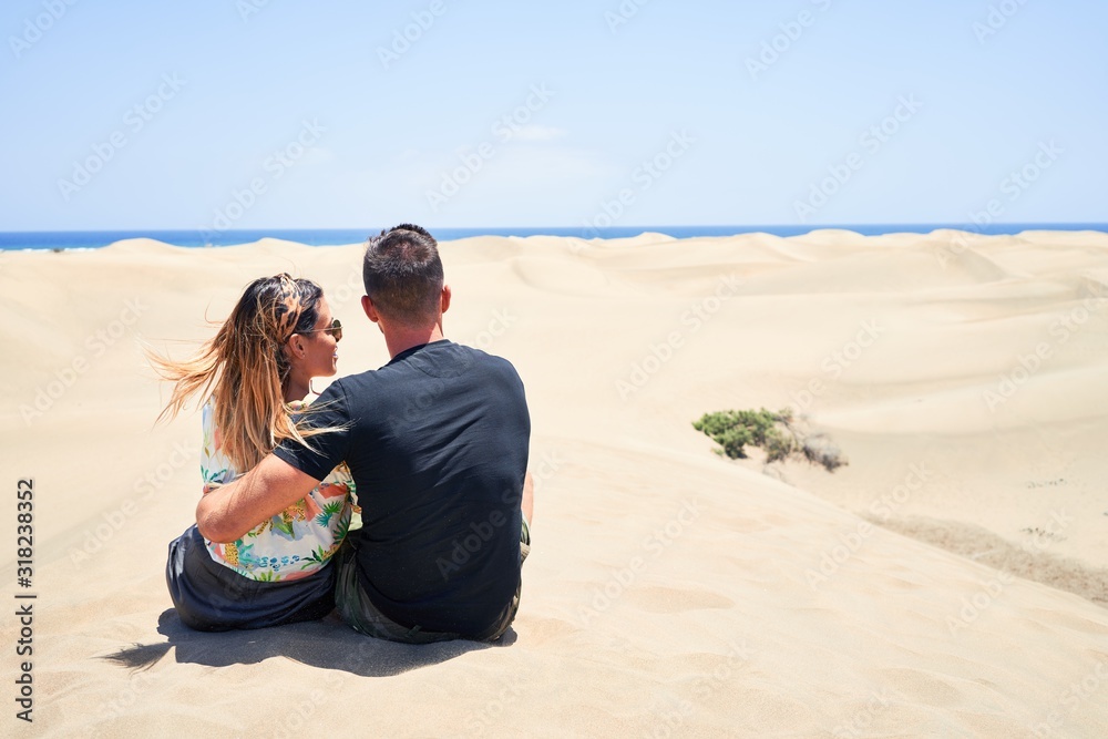 Young beautiful couple  at sitting backwards and hugging at the beach