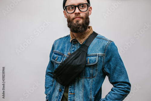 Obraz na płótnie Handsome hipster guy with beard wearing blue denim jacket and waist bag