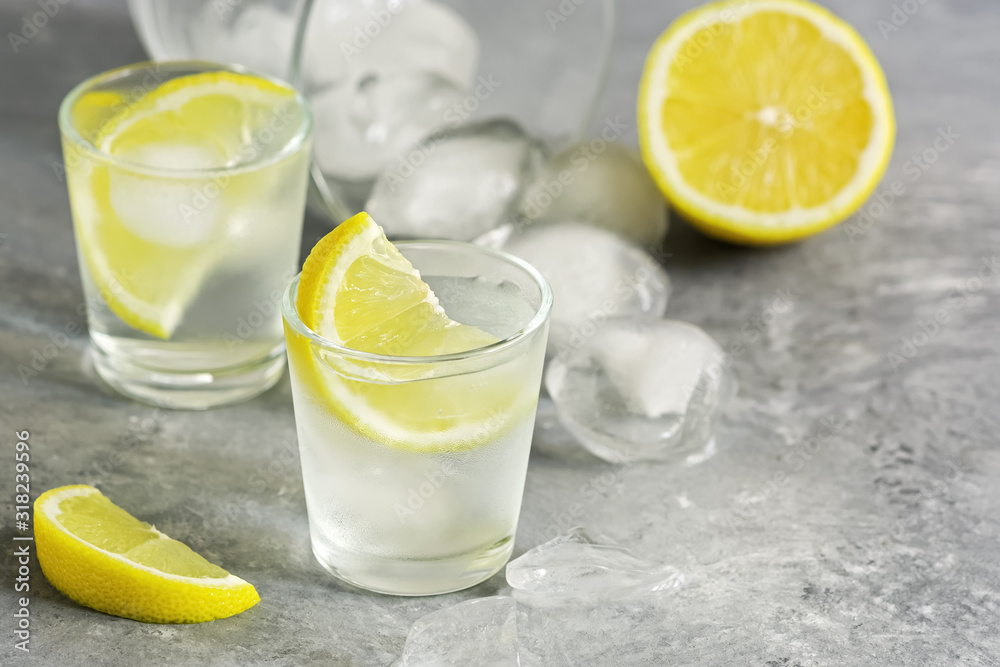Vodka shot glass with ice and juicy lemon slices on a gray concrete background. Traditional Russian alcohol. Selective focus, copy space. Vodka shot glass with ice and juicy lemon slices on a gray concrete background. Traditional Russian alcohol. Selective focus, copy space.