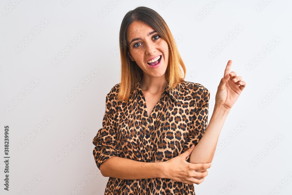 Beautiful redhead woman wearing elegant animal print shirt over isolated background with a big smile on face, pointing with hand and finger to the side looking at the camera. Beautiful redhead woman wearing elegant animal print shirt over isolated background with a big smile on face, pointing with hand and finger to the side looking at the camera.