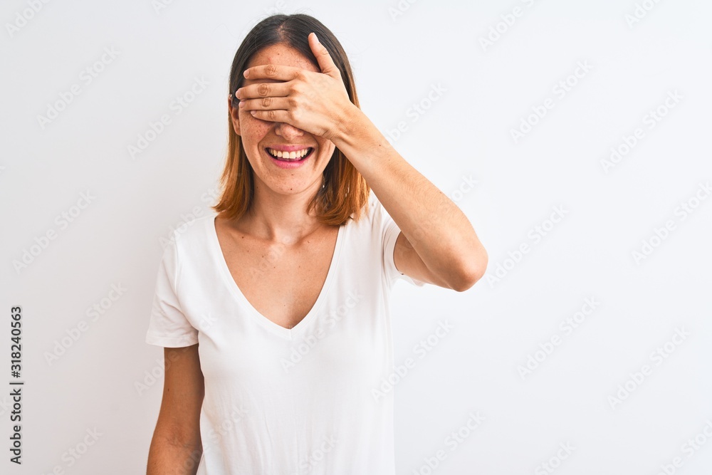 Beautiful redhead woman wearing casual white t-shirt over isolated background smiling and laughing with hand on face covering eyes for surprise. Blind concept. Beautiful redhead woman wearing casual white t-shirt over isolated background smiling and laughing with hand on face covering eyes for surprise. Blind concept.