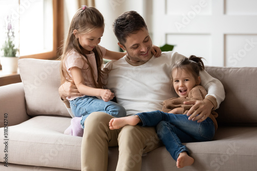 Loving father relax cuddle with little daughters on couch