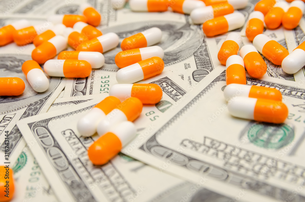 A lot of white and orange tablets on the background of dollar bills close-up. Concept of insurance, medicine