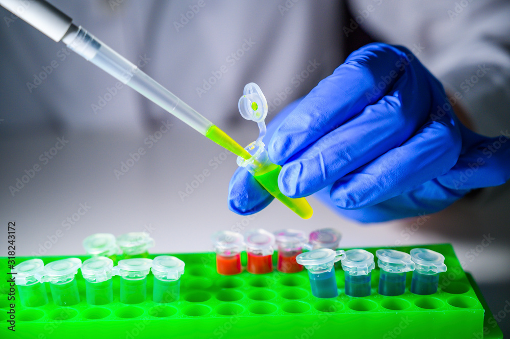 Scientist working with green solution in eppendorf tube and pipette for biomedical research with tube rack on a white bench Scientist working with green solution in eppendorf tube and pipette for biomedical research with tube rack on a white bench