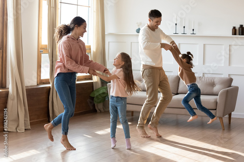 Happy parents dancing with small daughters in living room