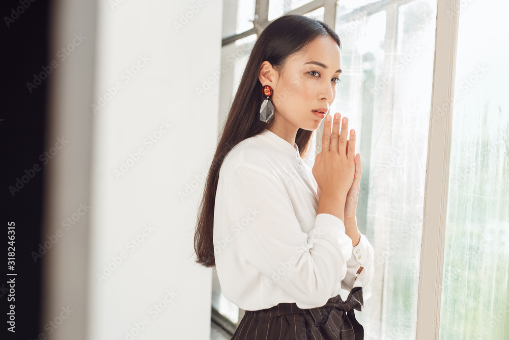 Freestyle. Young woman standing looking out the window hands in prayer with hope Freestyle. Young woman standing looking out the window hands in prayer with hope