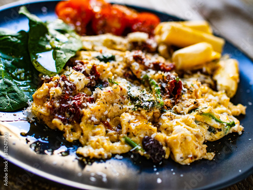 Breakfast - scrambled eggs with vegetables and grissini on wooden background