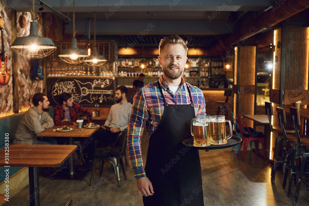 Bearded waiter with a tray of glasses of beer against the background of a pub bar - obrazy, fototapety, plakaty 