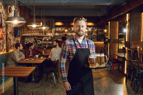 Bearded waiter with a tray of glasses of beer against the background of a pub bar photo