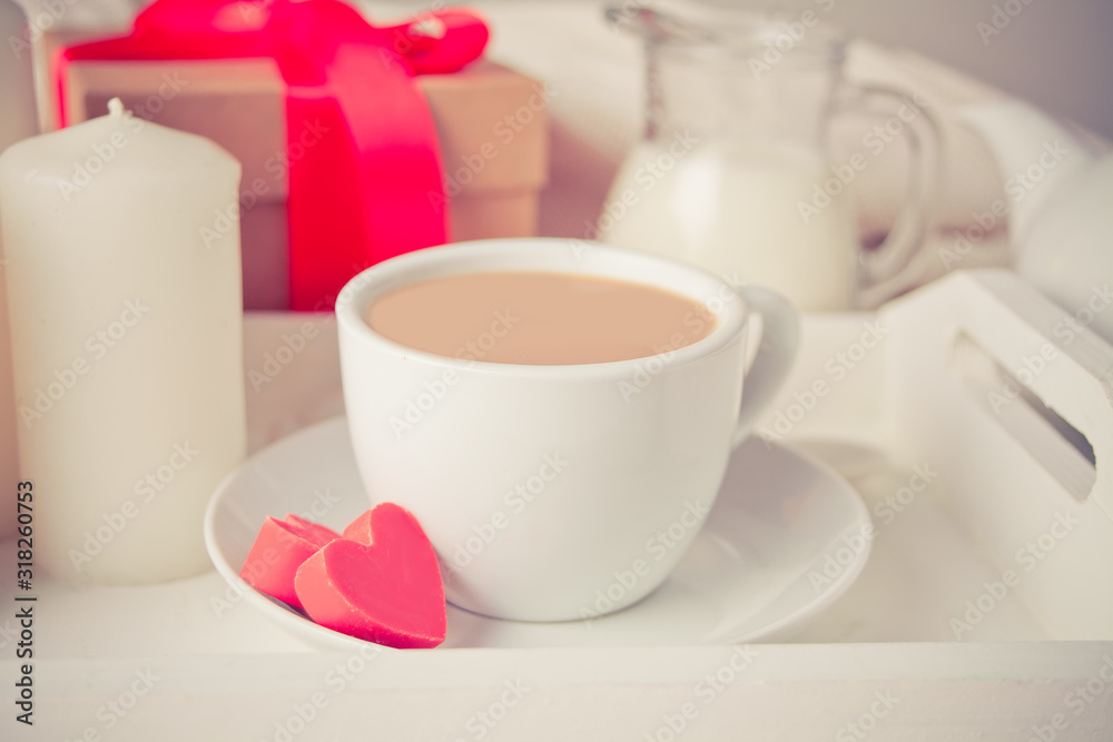Cup of coffee and a heart shaped red chocolate candies with gift box on the white tray