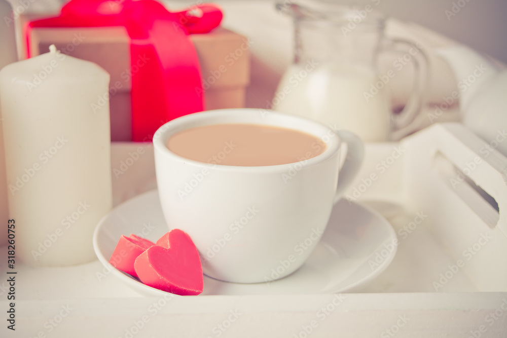 Cup of coffee and a heart shaped red chocolate candies with gift box on the white tray Cup of coffee and a heart shaped red chocolate candies with gift box on the white tray