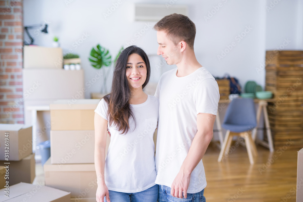 Young beautiful couple standing at new home around cardboard boxes Young beautiful couple standing at new home around cardboard boxes