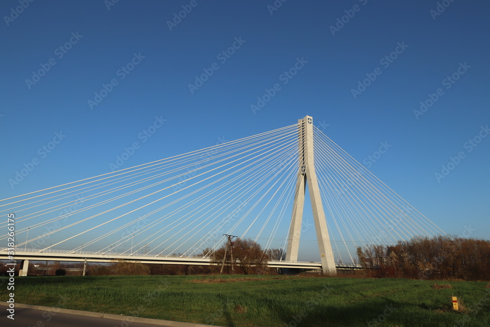 Fototapeta premium Rzeszow, Poland - 9 9 2018: Suspended road bridge across the Wislok River. Metal construction technological structure. Modern architecture. A white cross on a blue background is a symbol of the city