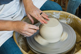 a caucasian woman trimming the base of an unfinished clay pot on a pottery wheel close up and adding detail work to the bottom