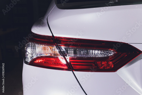 Close up of taillight detail of modern luxury sportscar with reflection on white paint after wash wax. Rear view of supercar break lights. Concept of car detailing and paint protection background.