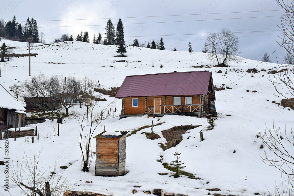 An old wooden house with a wooden gazebo stands on the side of a snowy mountain. Winter landscape, cloudy weather. Wooden house for winter holidays in the Carpathians. An old wooden house with a wooden gazebo stands on the side of a snowy mountain. Winter landscape, cloudy weather. Wooden house for winter holidays in the Carpathians.