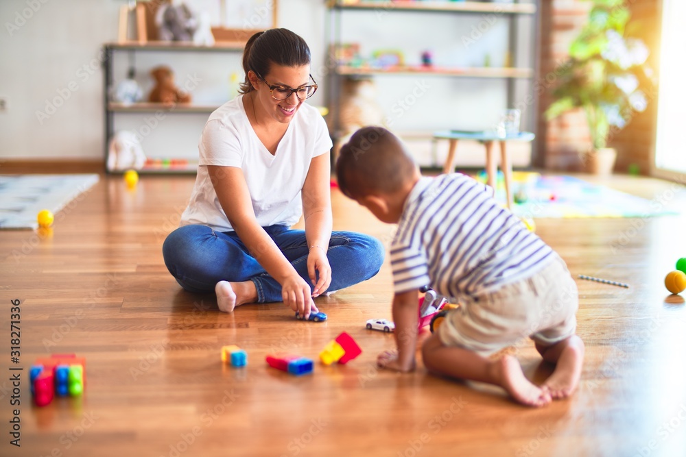 Fototapeta premium Beautiful teacher and toddler boy playing with tractor and cars at kindergarten
