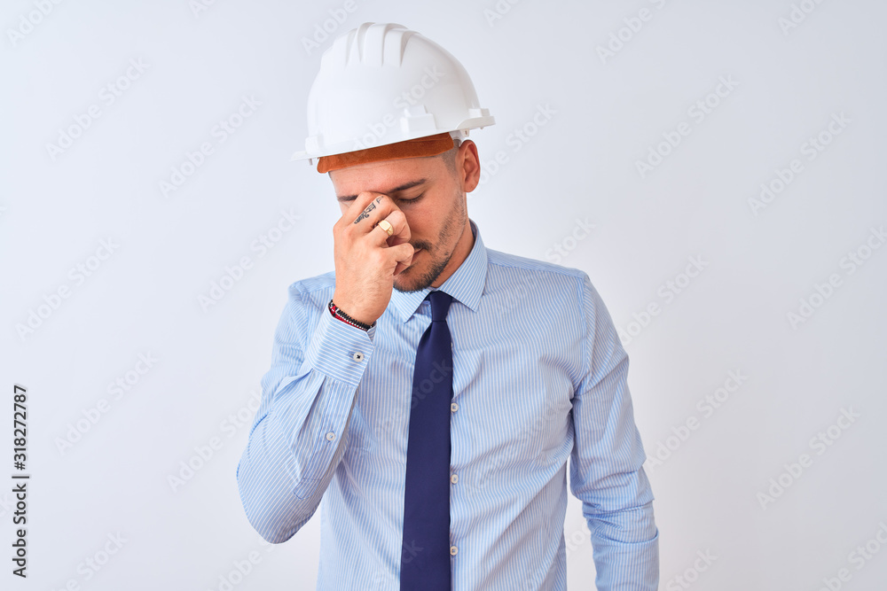 Young business man wearing contractor safety helmet over isolated background tired rubbing nose and eyes feeling fatigue and headache. Stress and frustration concept.