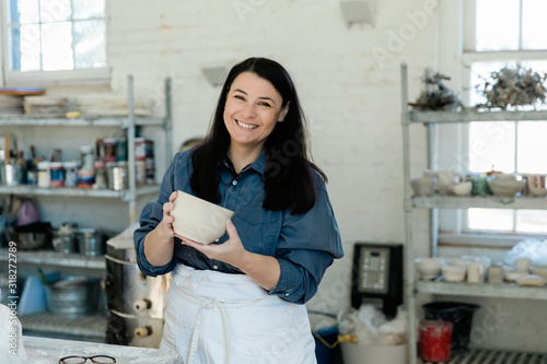 smiling Creative Pottery Cermanic female artist holding a piece of unfinished clay pottery in an art loft studio photo