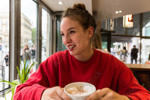 Young Woman in Coffee Shop Holding Cappuccino Mug Smiling and Looking Away