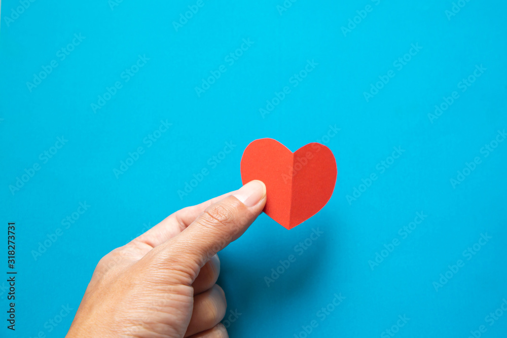 Hand holding red heart paper on blue background Hand holding red heart paper on blue background