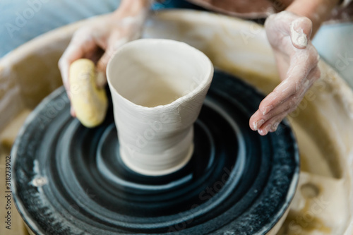 And unbalanced and lopsided imperfect clay pot being made on a pottery wheel by a student who is learning how to throw pots on a pottery wheel