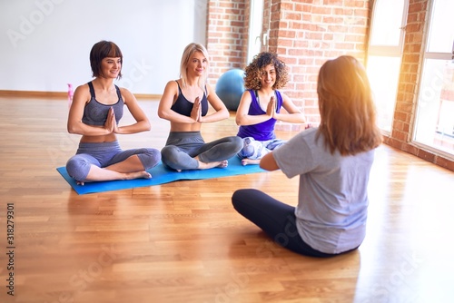 Young beautiful group of sportswomen sitting on mat practicing yoga. Coach teaching lotus pose at gym
