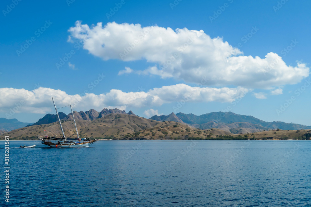 Fototapeta premium A view on idyllic island in Komodo National Park, Indonesia. There are few clouds above the island. Calm and clear surface of the sea. Island hoping. Perfect day for sailing