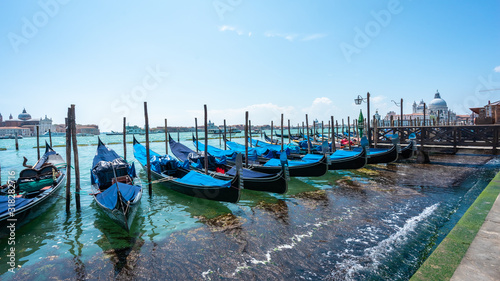 Gondolas on the Grand Canal pier in Venice from the side of the Doges palace. San Giorgio Maggiore Island background. Gondolas jetty. The row of  beautiful  Venetian gondolas mooring on berth Panorama © GenоМ.