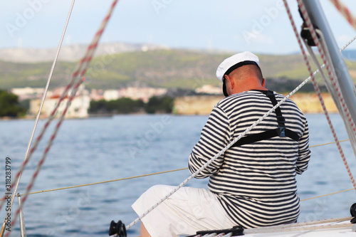 Yachtsman in marine clothing looking into the distance sitting on board a sailing yacht. Sea fishing from the ship. Peaceful state at summer holidays. Travel experienced person around the world