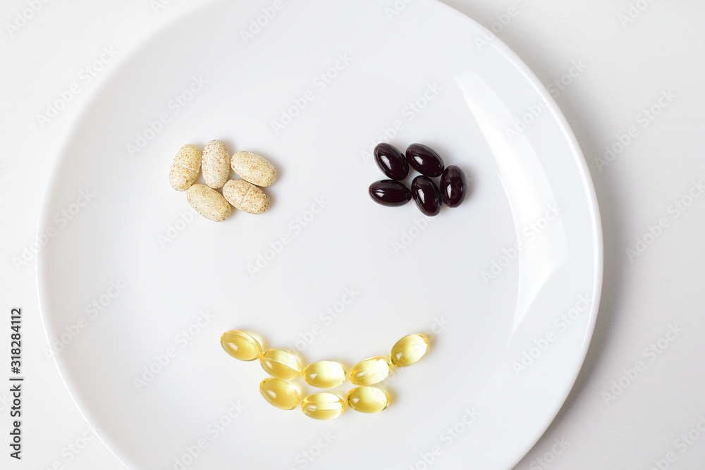 Astaxanthin, multivitamins and fish oil in a shape of smile on a white plate. Astaxanthin, multivitamins and fish oil in a shape of smile on a white plate.