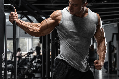 Muscular man showing muscles in gym. Strong male working out