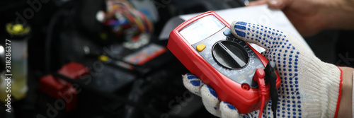 Close-up of male hands checking voltage of automobile battery under hood machine with accuracy. Automechanic using modern utility. Automotive checkup concept