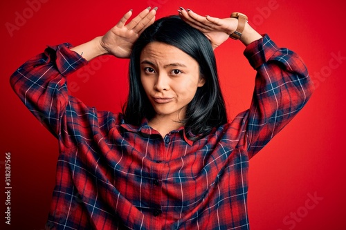 Young beautiful chinese woman wearing casual shirt over isolated red background Doing bunny ears gesture with hands palms looking cynical and skeptical. Easter rabbit concept. photo