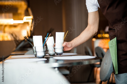 Waiter puts the glasses on table in cafe