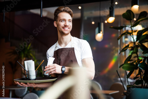 Nice young waiter working in cafe and posing for camera photo