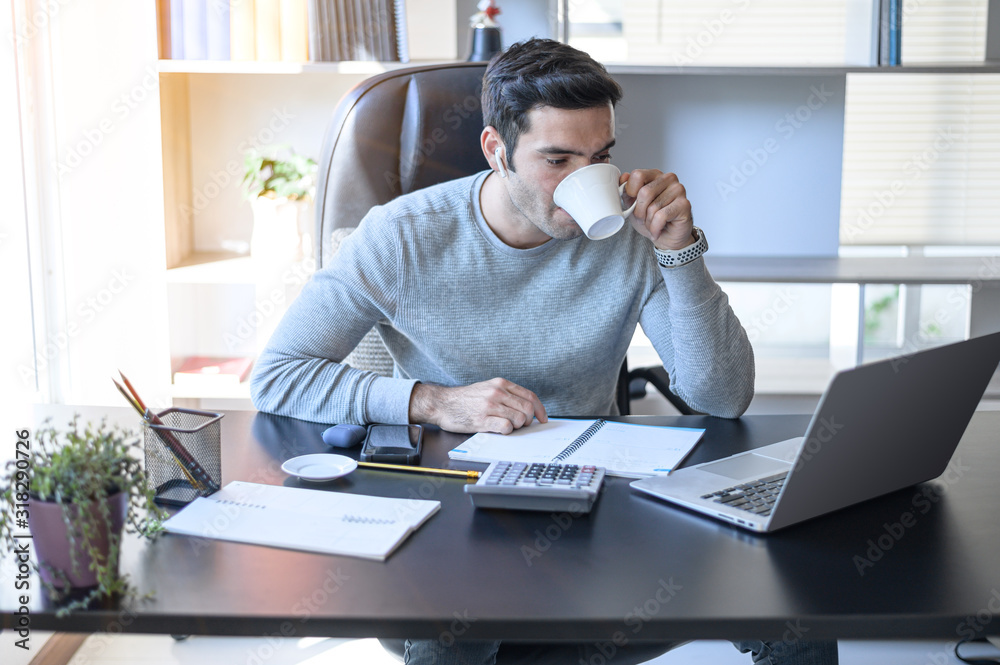 A young man working at a desk with a laptop. Calculator, notepad, pencil, pen and cup of coffee on the side. A young man working at a desk with a laptop. Calculator, notepad, pencil, pen and cup of coffee on the side.