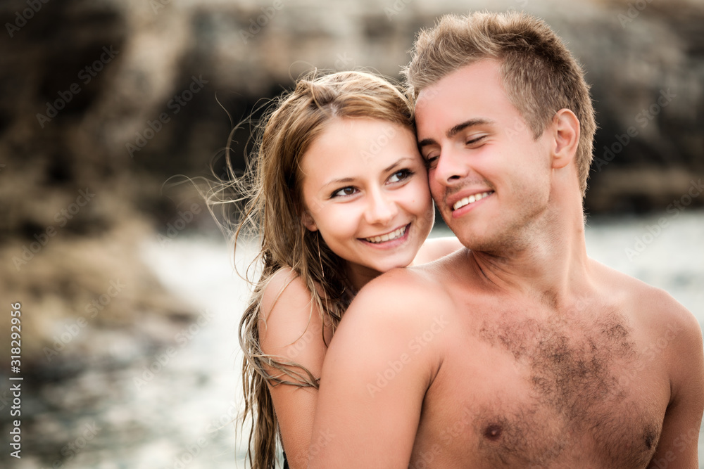 Young beautiful smiling woman embracing from back her happy boyfriend with natural rocks at background on clear summer day. Travelling, vacations, romantic weekend, honeymoon concept Young beautiful smiling woman embracing from back her happy boyfriend with natural rocks at background on clear summer day. Travelling, vacations, romantic weekend, honeymoon concept